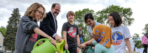 Northeast Middle School students and MWMO Board Chair Kevin Reich pour water on a rain garden plant at a ceremony.